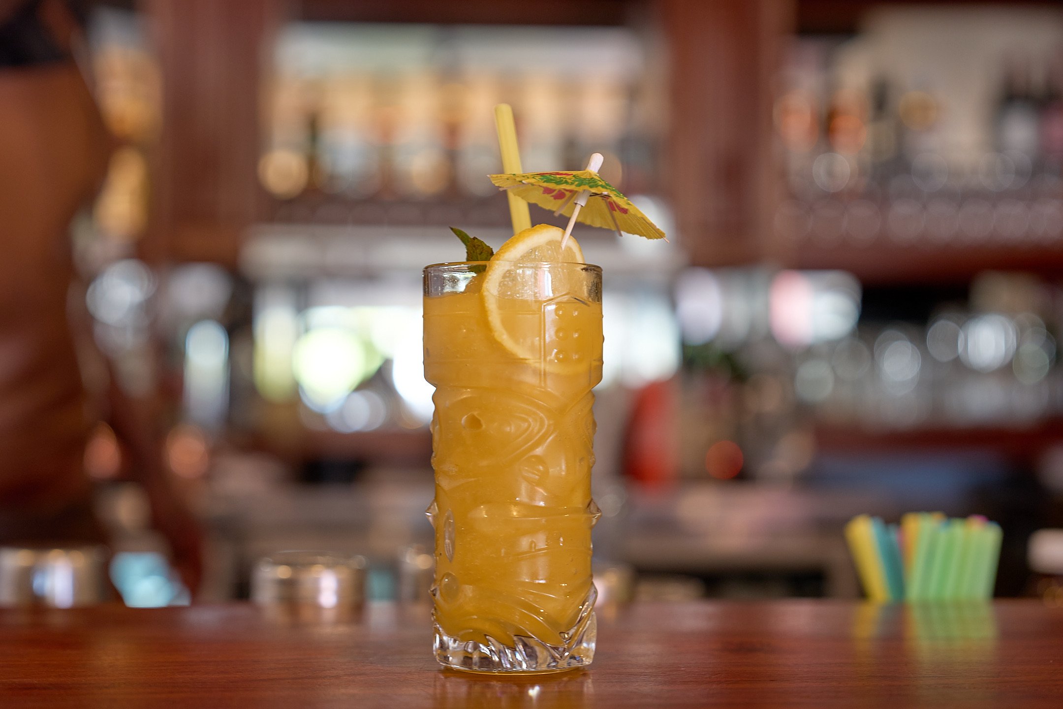 Tiki-glass cocktail with lemon wheel, mint and paper umbrella